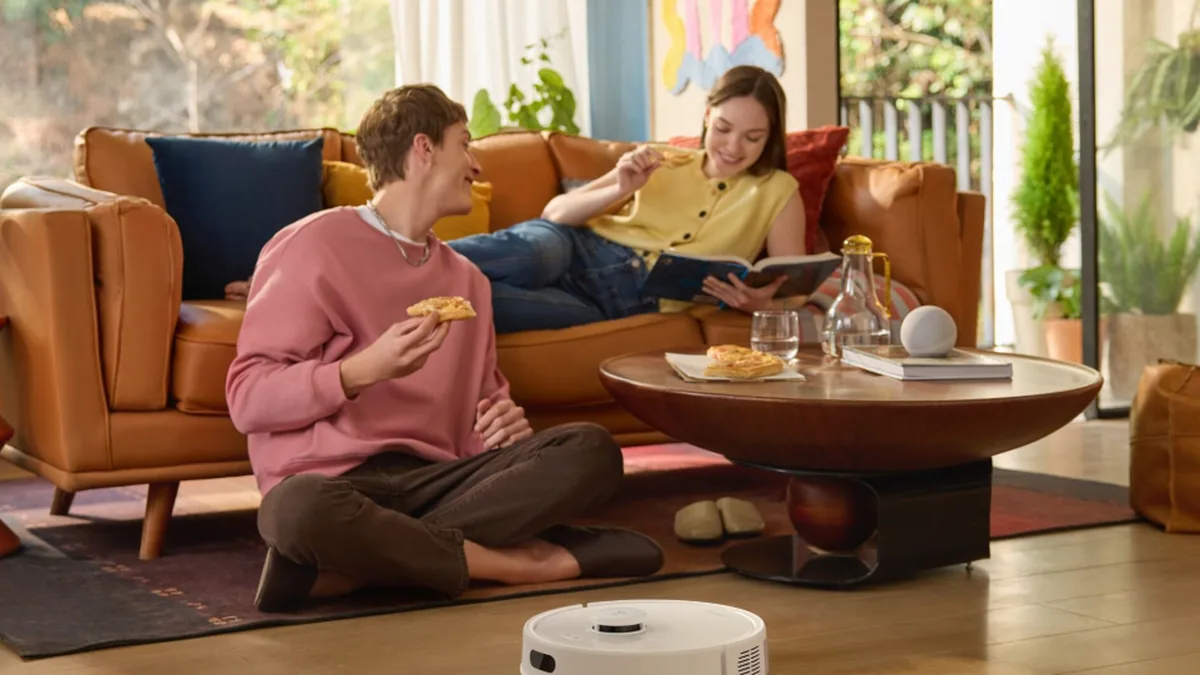 Aspirateur robot en fonctionnement dans un salon pendant que la famille déjeune