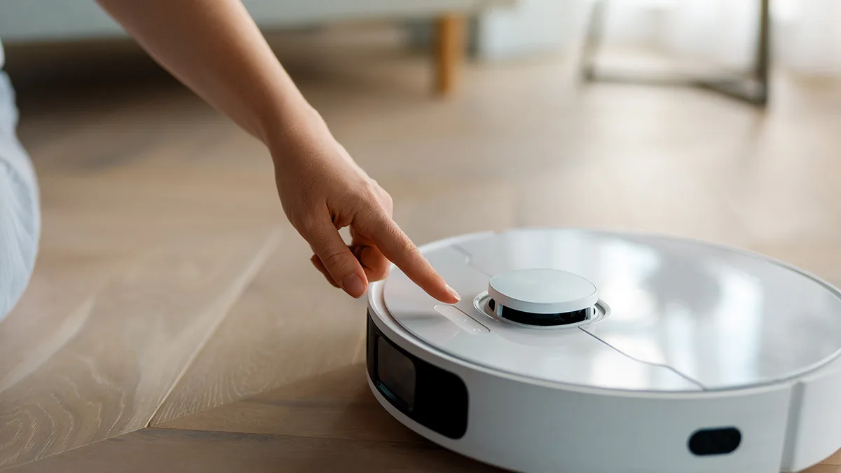 Doigt appuyant sur le bouton physique d'un aspirateur robot